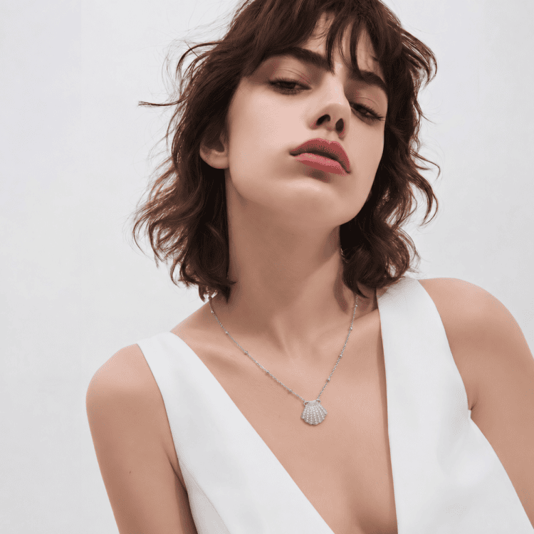 Ανακάλυψε το Maris Necklace, ένα κομψό κολιέ από ανοξείδωτο ατσάλι με χρυσό φινίρισμα, μενταγιόν σε σχήμα κοχυλιού και λαμπερά λευκά ζιργκόν