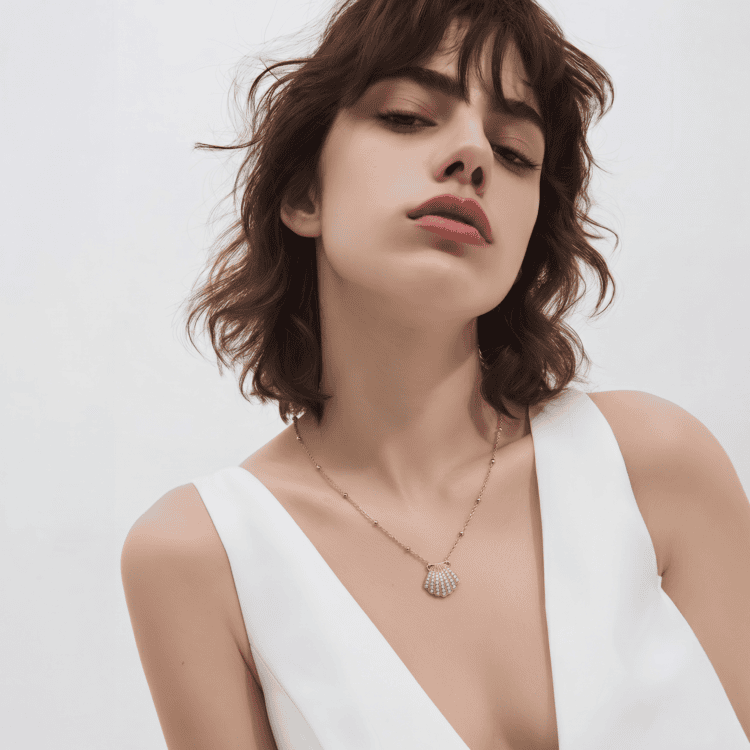 Ανακάλυψε το Maris Necklace, ένα κομψό κολιέ από ανοξείδωτο ατσάλι με χρυσό φινίρισμα, μενταγιόν σε σχήμα κοχυλιού και λαμπερά λευκά ζιργκόν